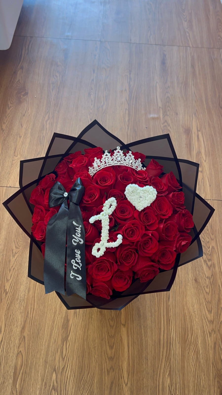 Romantic 'I Love You!' 50-rose deep red Ecuadorian round rose bouquet with sparkling crystal crown tiara, elegant cursive letter 'L' crafted from white baby's breath across blooms, small baby's breath heart accent, 'I Love You!' silver script black satin ribbon bow, and sleek black geometric paper wrap - luxury personalized love declaration arrangement by FridAndre Florals