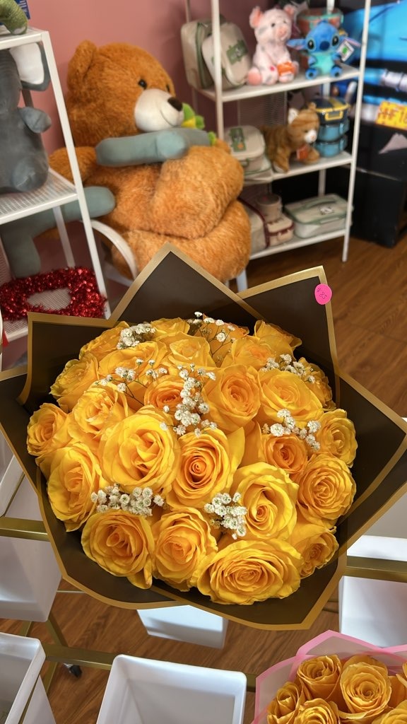 Lush round bouquet of bright yellow Ecuadorian roses accented with delicate white baby's breath in sleek black and gold star-point wrap by FridAndre Florals