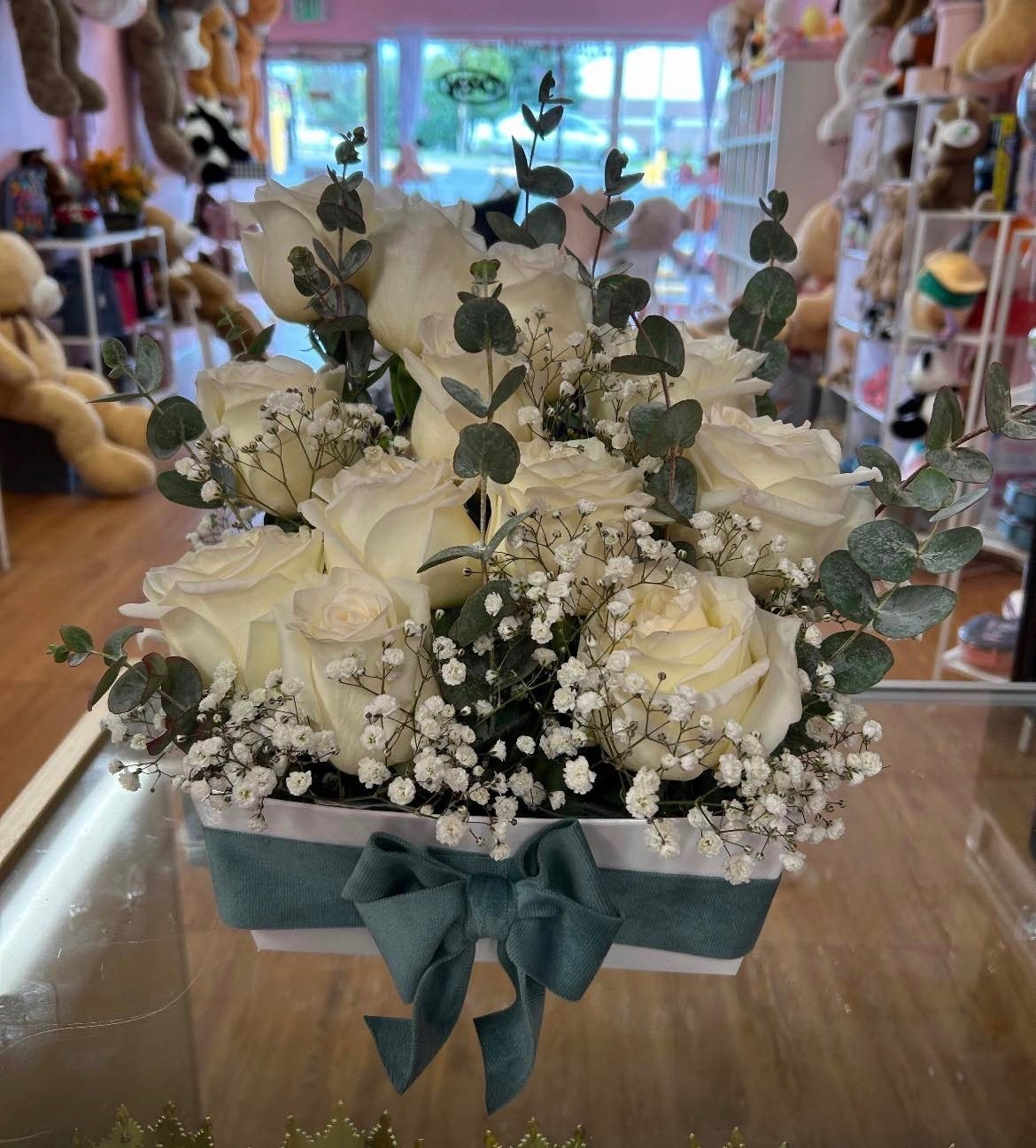 Elegant white Ecuadorian rose box arrangement with fresh eucalyptus leaves, delicate white baby's breath filler, and teal blue satin ribbon bow - compact luxury gift box