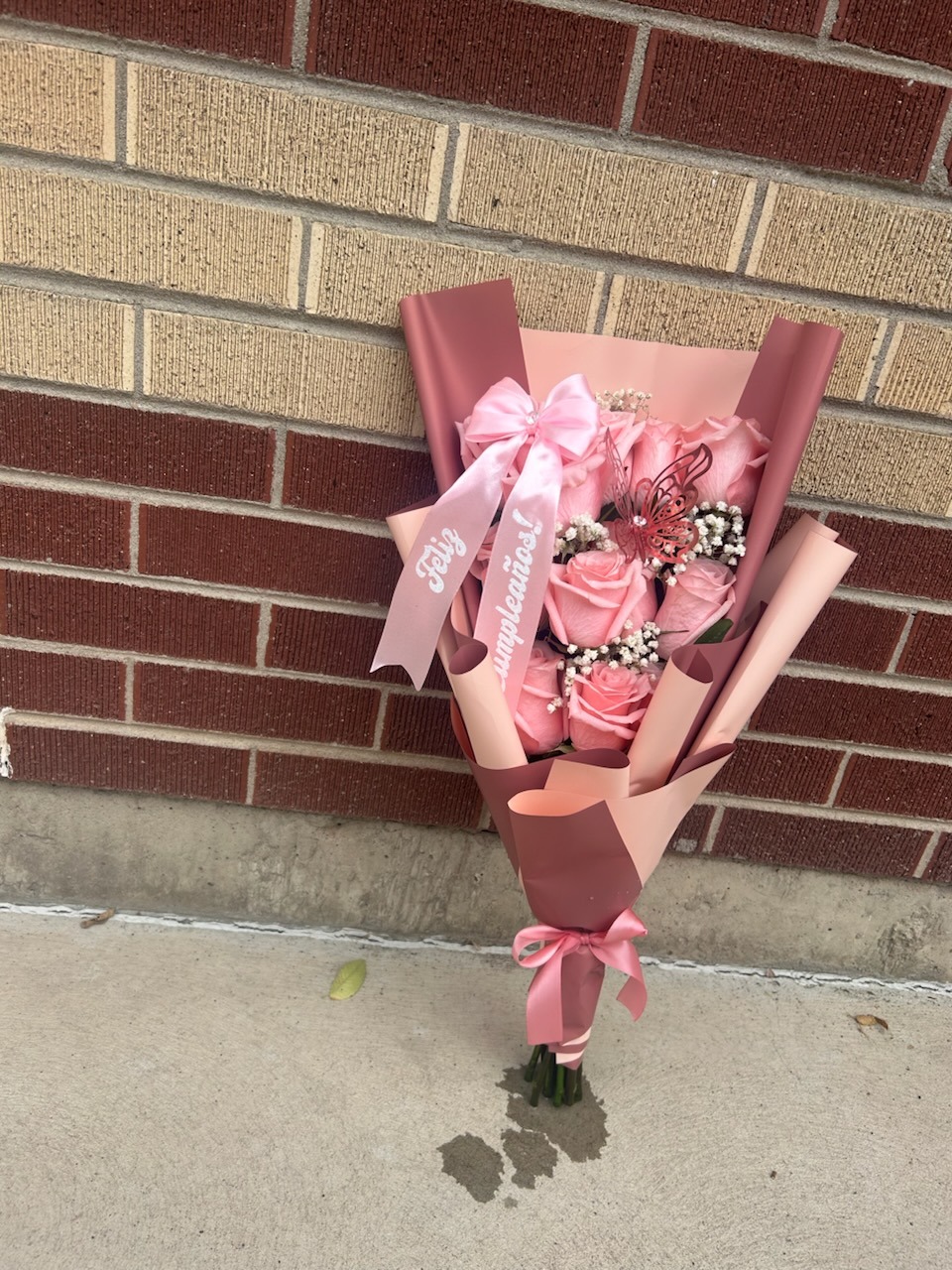 Elegant 'Feliz Cumpleaños!' 12-rose soft pink Ecuadorian rose bouquet with white baby's breath filler, dark pink laser-cut butterfly decoration, pink satin ribbon bow, and rose-mauve geometric paper wrap - compact birthday celebration arrangement by FridAndre Florals