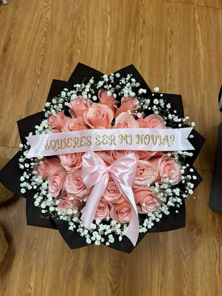 Romantic '¿Quieres Ser Mi Novia?' 25-rose pink Ecuadorian rose bouquet with white baby's breath border, elegant pink satin ribbon bow, and gold-lettered proposal banner - wrapped in black geometric paper