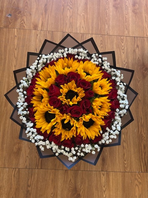 Stunning concentric circular floral arrangement of bright golden sunflowers and deep red roses framed with white baby's breath in black star-point wrap by FridAndre Florals