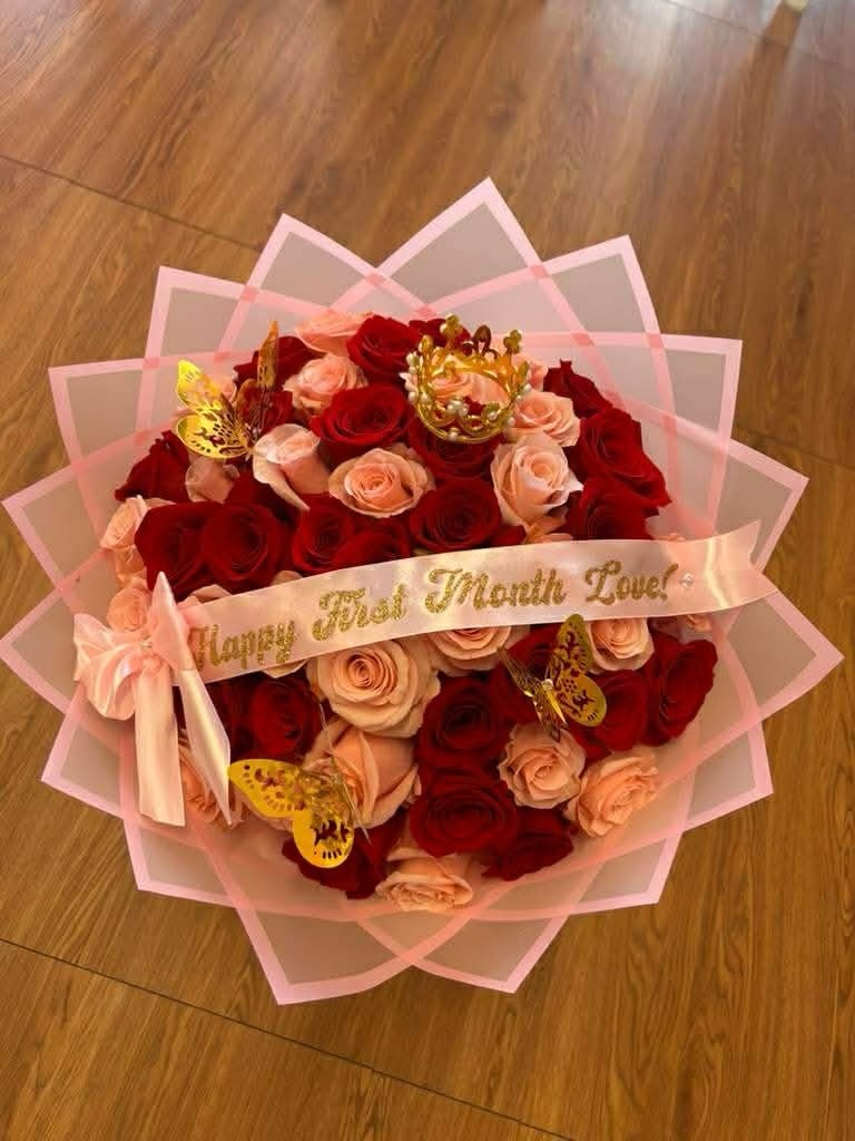 Stunning 'Happy First Month Love!' 50-rose red and pink Ecuadorian rose bouquet with crystal crown tiara, golden laser-cut butterfly decorations, baby's breath border, gold-lettered ribbon bow, and elegant pink geometric paper wrap - luxury anniversary arrangement