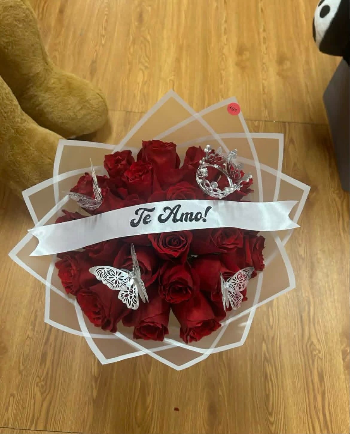 Romantic 'Te Amo!' 25-rose red Ecuadorian rose bouquet with sparkling crystal crown tiara, silver laser-cut butterfly decorations, elegant white geometric paper wrap, and 'Te Amo!' gold-glitter lettered satin ribbon bow - love declaration arrangement