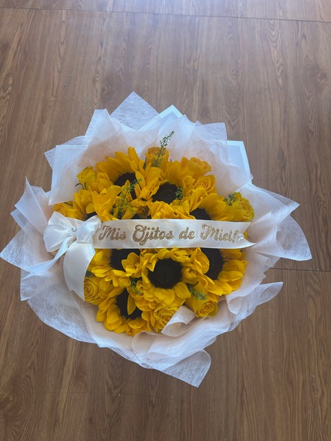 Vibrant 10-sunflower bouquet with yellow Ecuadorian roses, custom 'Mis Ojitos de Miel!' glitter ribbon, white bow, and delicate white star-point wrap by FridAndre Florals