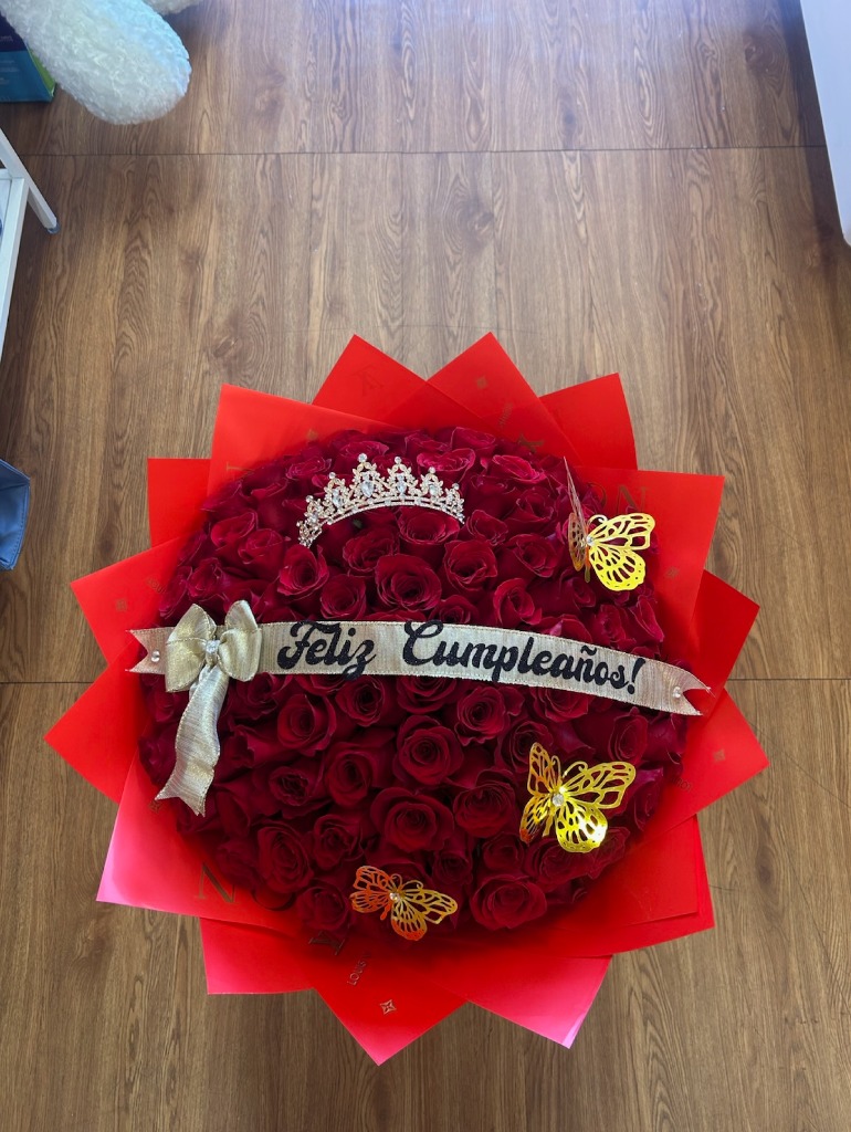 Stunning 'Feliz Cumpleaños!' 100-rose deep red Ecuadorian round rose bouquet with sparkling crystal crown tiara, three golden laser-cut butterfly decorations, 'Feliz Cumpleaños!' black satin ribbon bow with gold bow accent, and vibrant red star-point paper wrap - luxury birthday celebration arrangement by FridAndre Florals