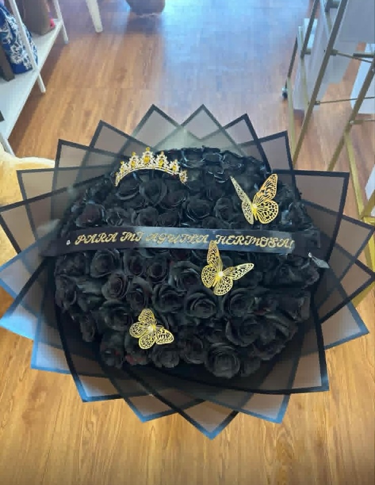 Dramatic 100-painted black rose bouquet with crystal crown tiara, golden laser-cut butterfly decorations, 'Para Mi Reina Hermosa' gold-lettered ribbon, and sleek black geometric paper wrap - luxury gothic romantic arrangement