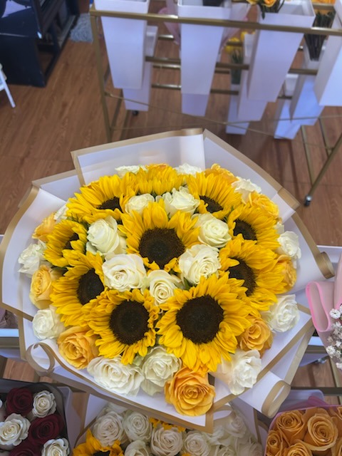 Radiant mixed bouquet of bright golden sunflowers, pristine white Ecuadorian roses, and soft peach roses wrapped in layered white and gold paper by FridAndre Florals