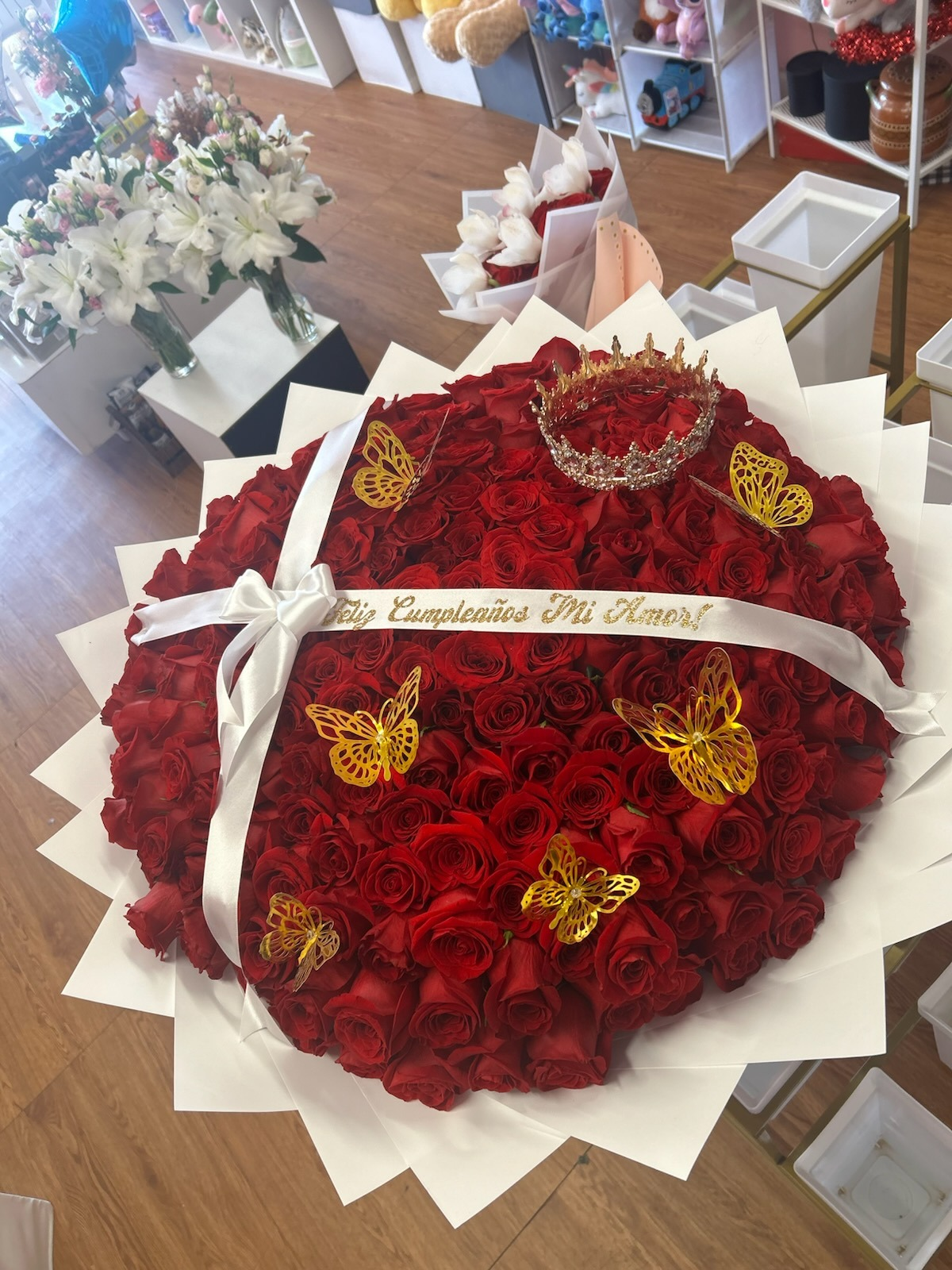 Massive heart-shaped 200-rose deep red Ecuadorian rose bouquet with sparkling crystal crown tiara, five golden laser-cut butterfly decorations, 'Feliz Cumpleaños Mi Amor!' gold-glitter lettered white satin ribbon bow, and elegant white geometric paper wrap - ultra premium luxury birthday love declaration arrangement by FridAndre Florals