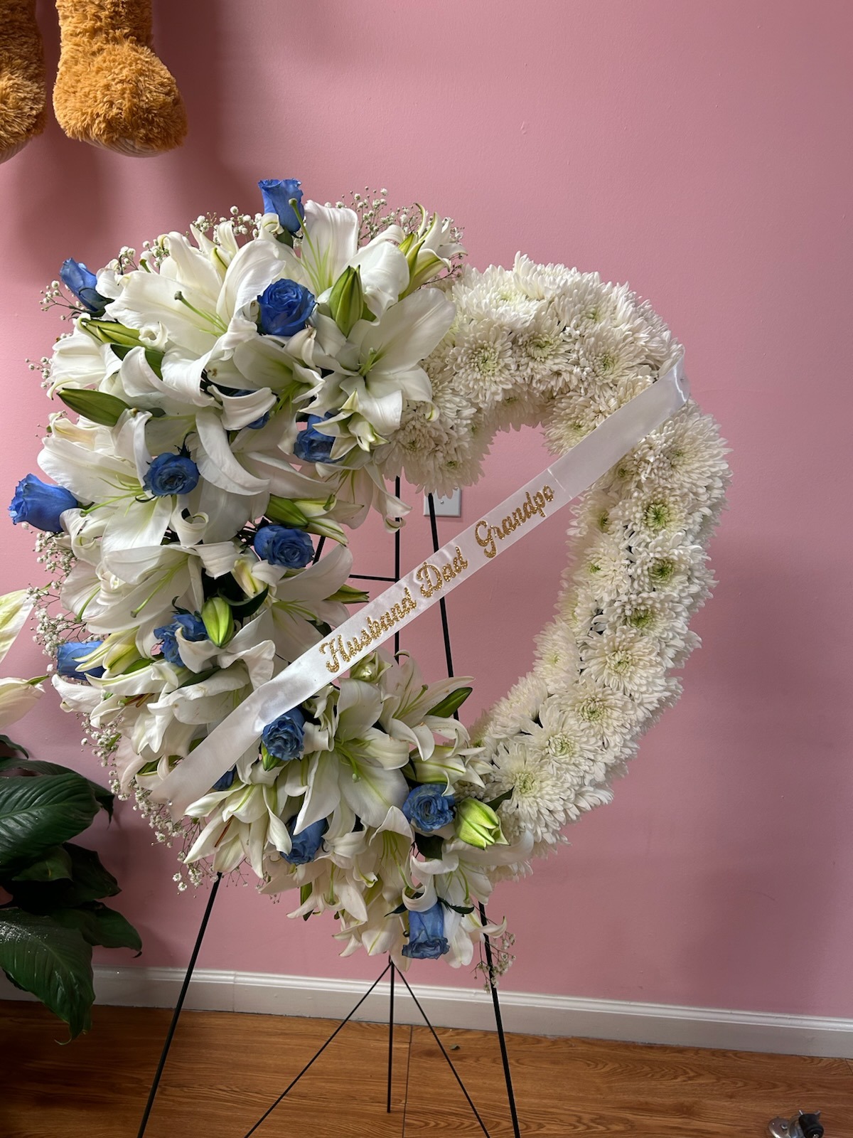 Large heart-shaped sympathy standing wreath with white lilies, blue roses, white chrysanthemums, baby's breath, and 'Husband Dad Grandpa' memorial ribbon - medium size