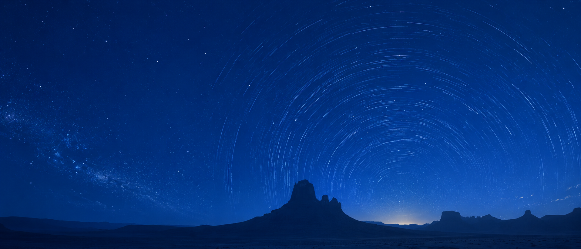 Star trails over desert landscape with mountain silhouette