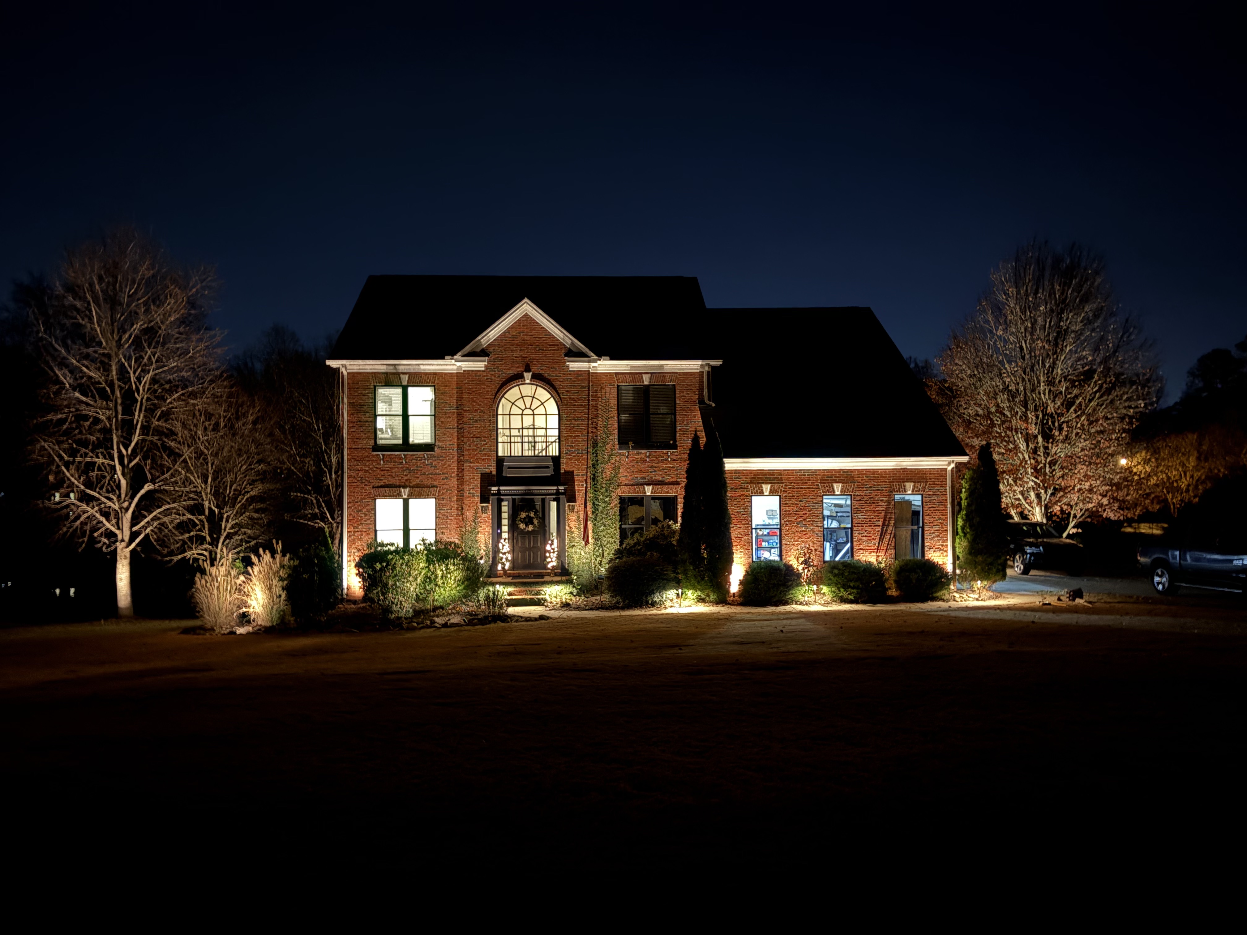 Two-story brick home architectural uplighting highlighting entry archways and rooflines in Simpsonville SC