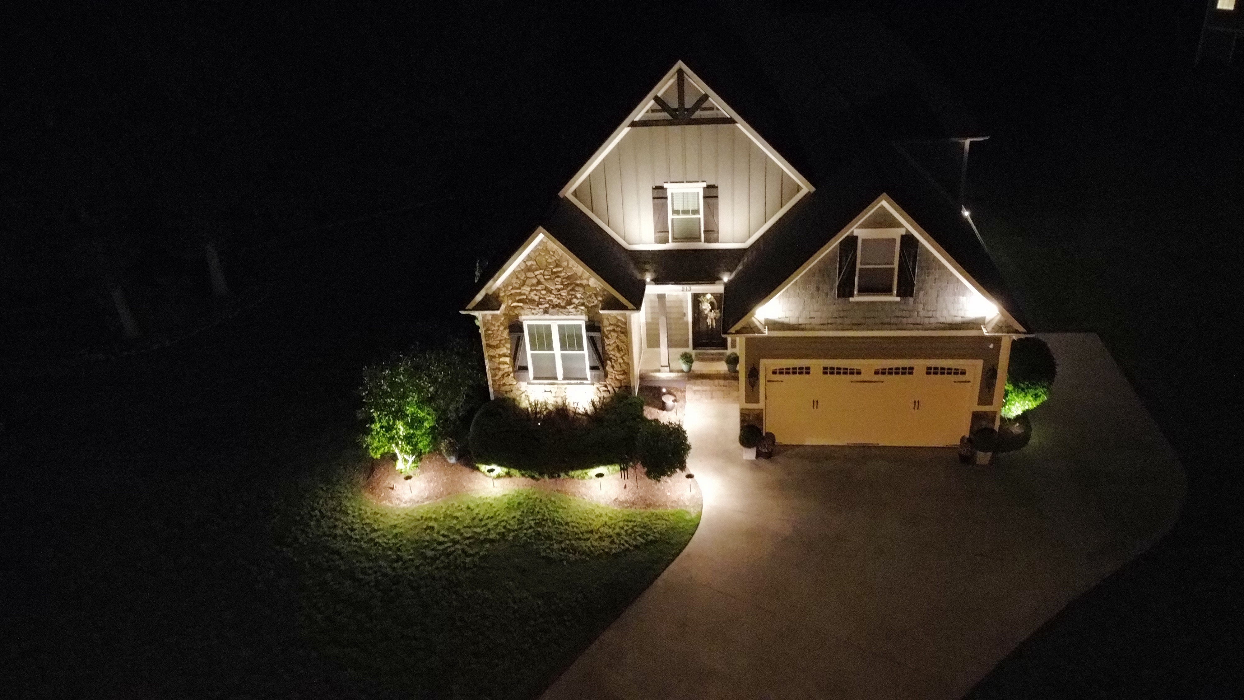 Aerial drone view of modern Craftsman residence front facade and walkway lighting in Upstate SC