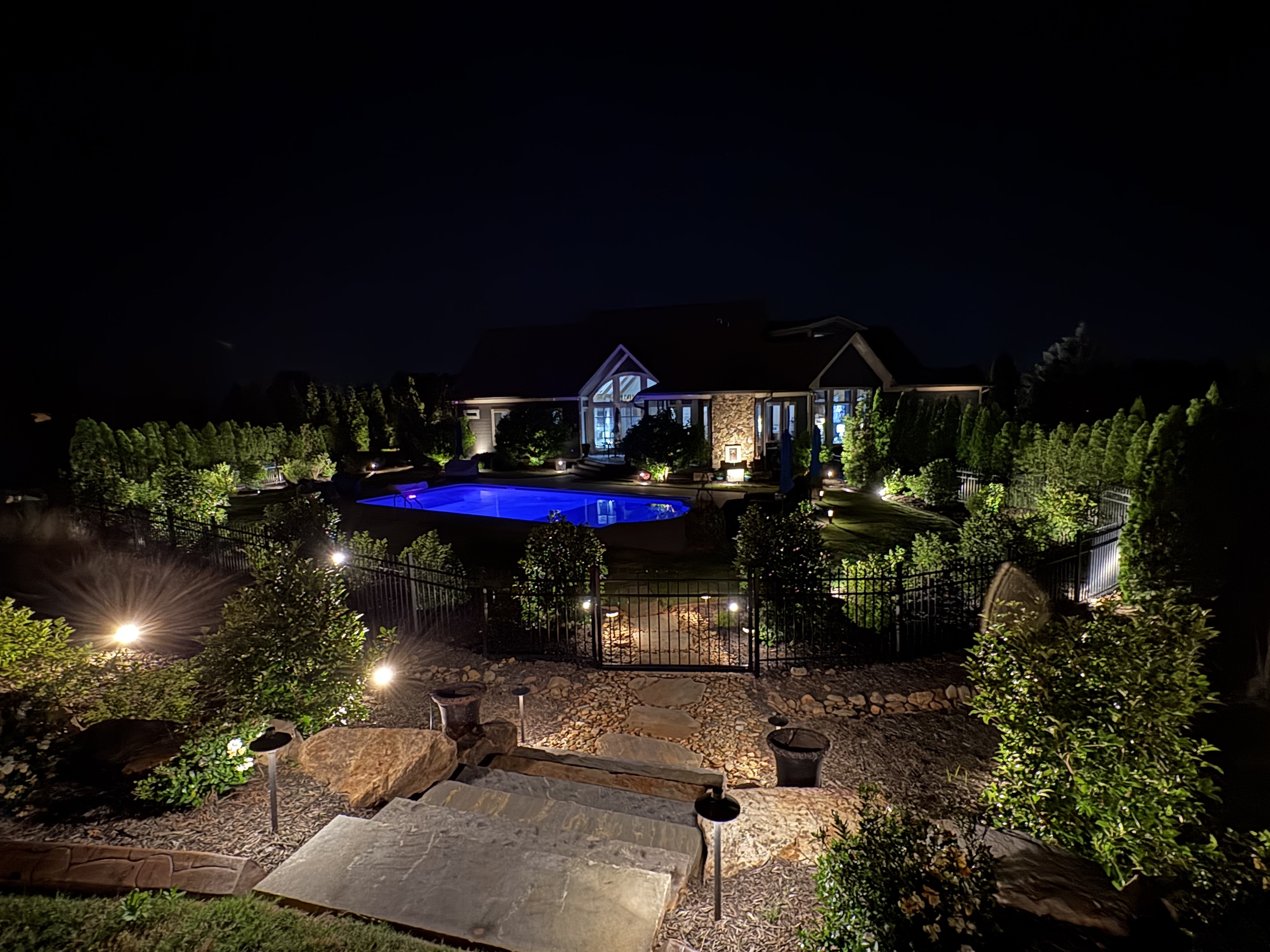 Resort style swimming pool, illuminated stone staircase, and outdoor patio terrace landscape lighting in Greenville SC