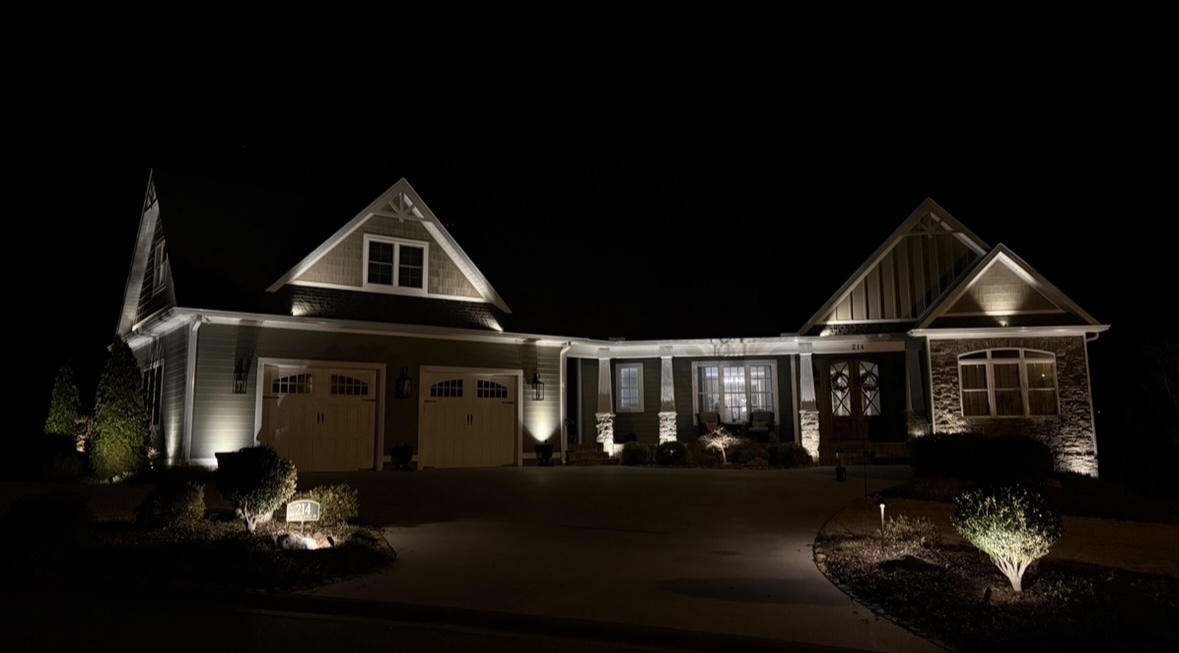 Broad front facade view of custom craftsman home with warm LED gable and column uplighting in Greenville SC
