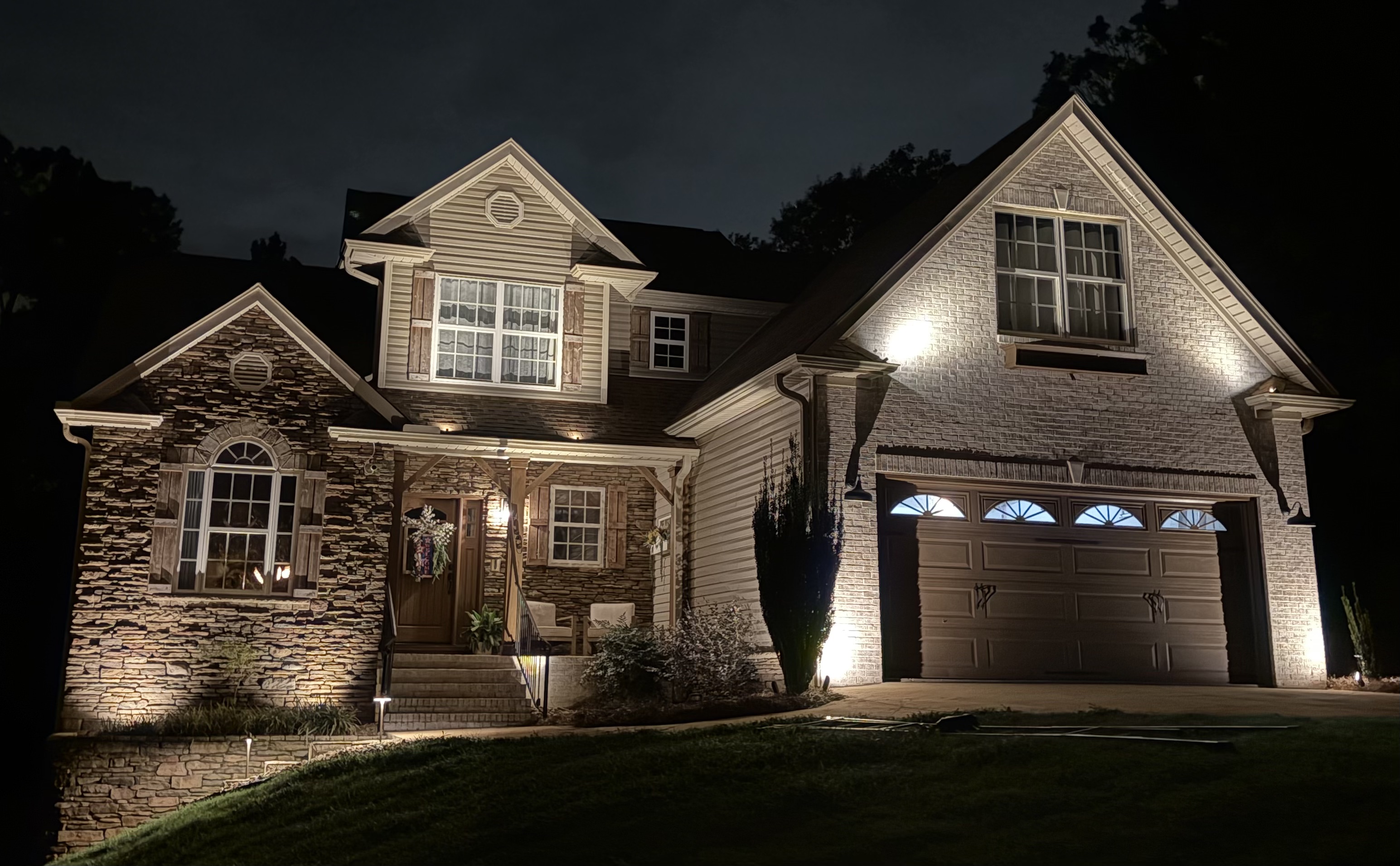Luxury two-story home with stone entry archway, garage facade wash lighting and garden path fixtures in Simpsonville SC