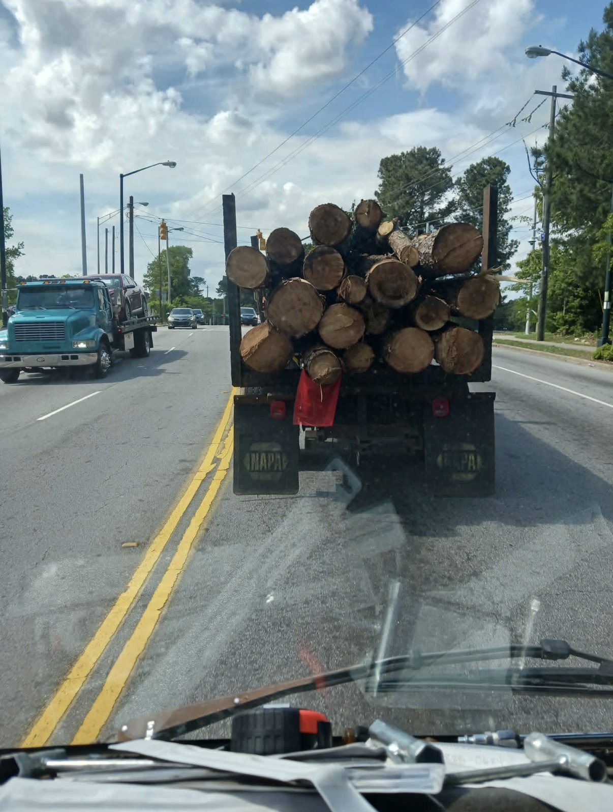 Flatbed log truck loaded with heavy cut tree logs being hauled by Shackleford Tree Service