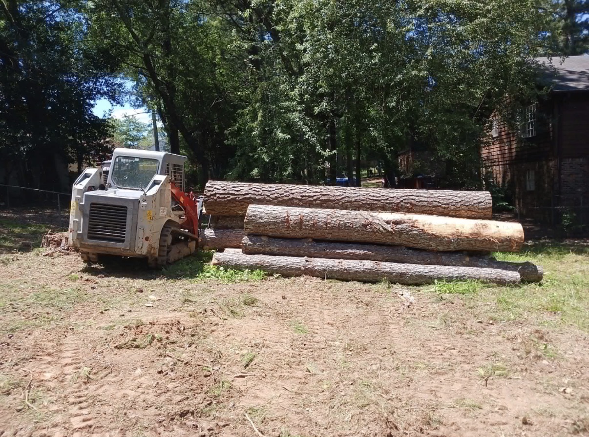 Skid steer loader with grapple attachment moving cut tree logs at a job site