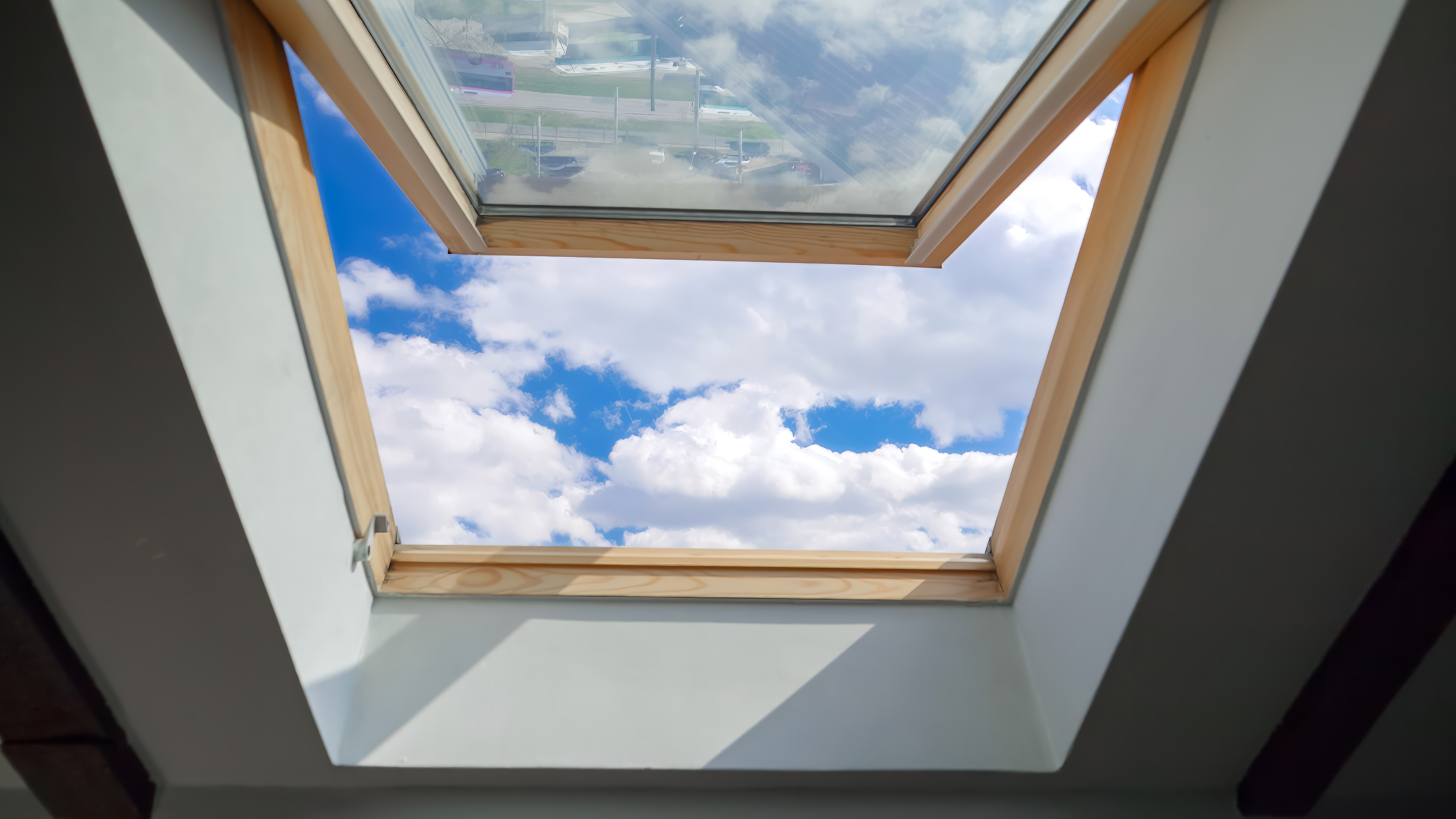 Open wooden-framed roof window with cloudy sky visible