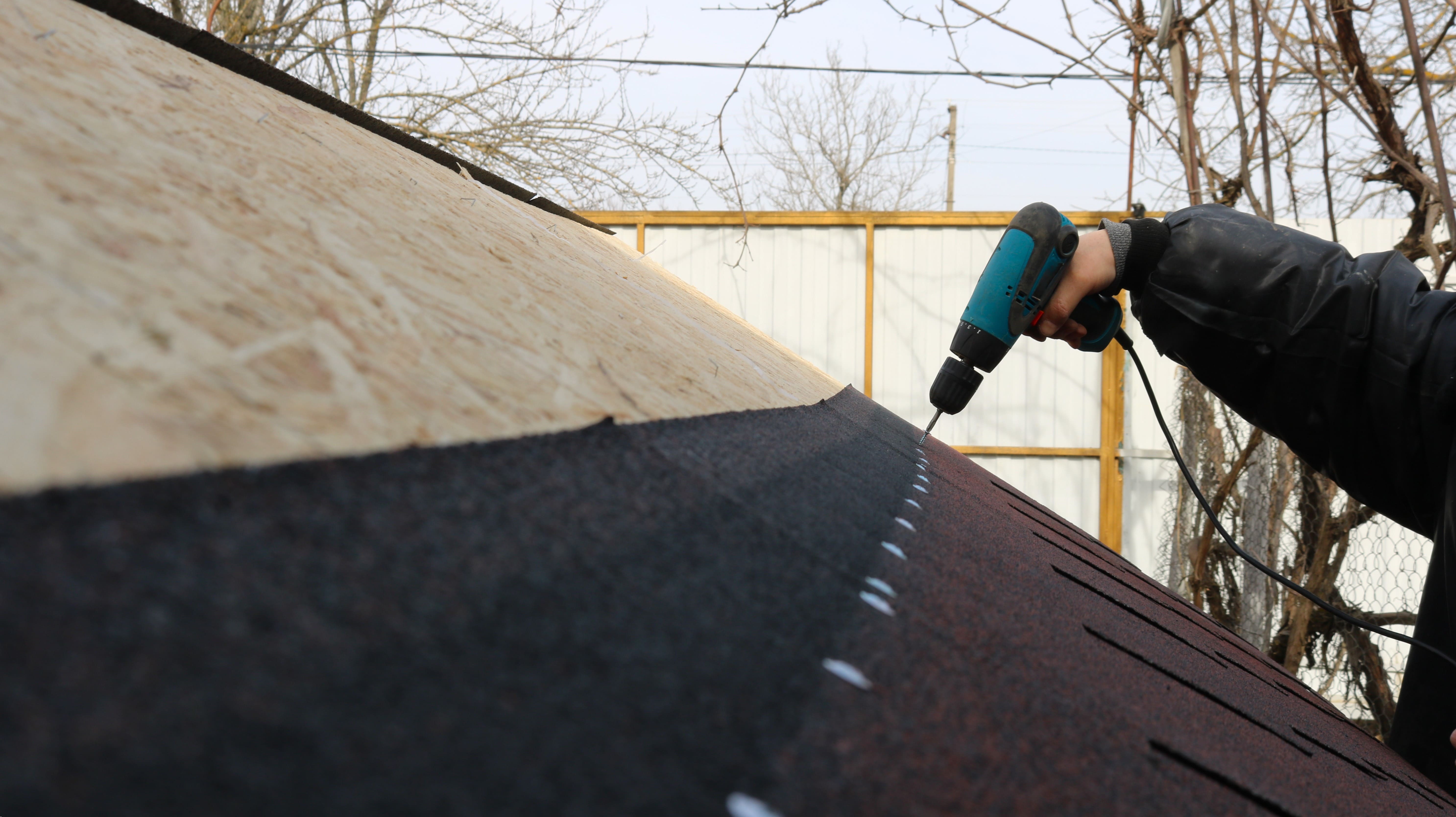 Roofer installing new roof covering with drill