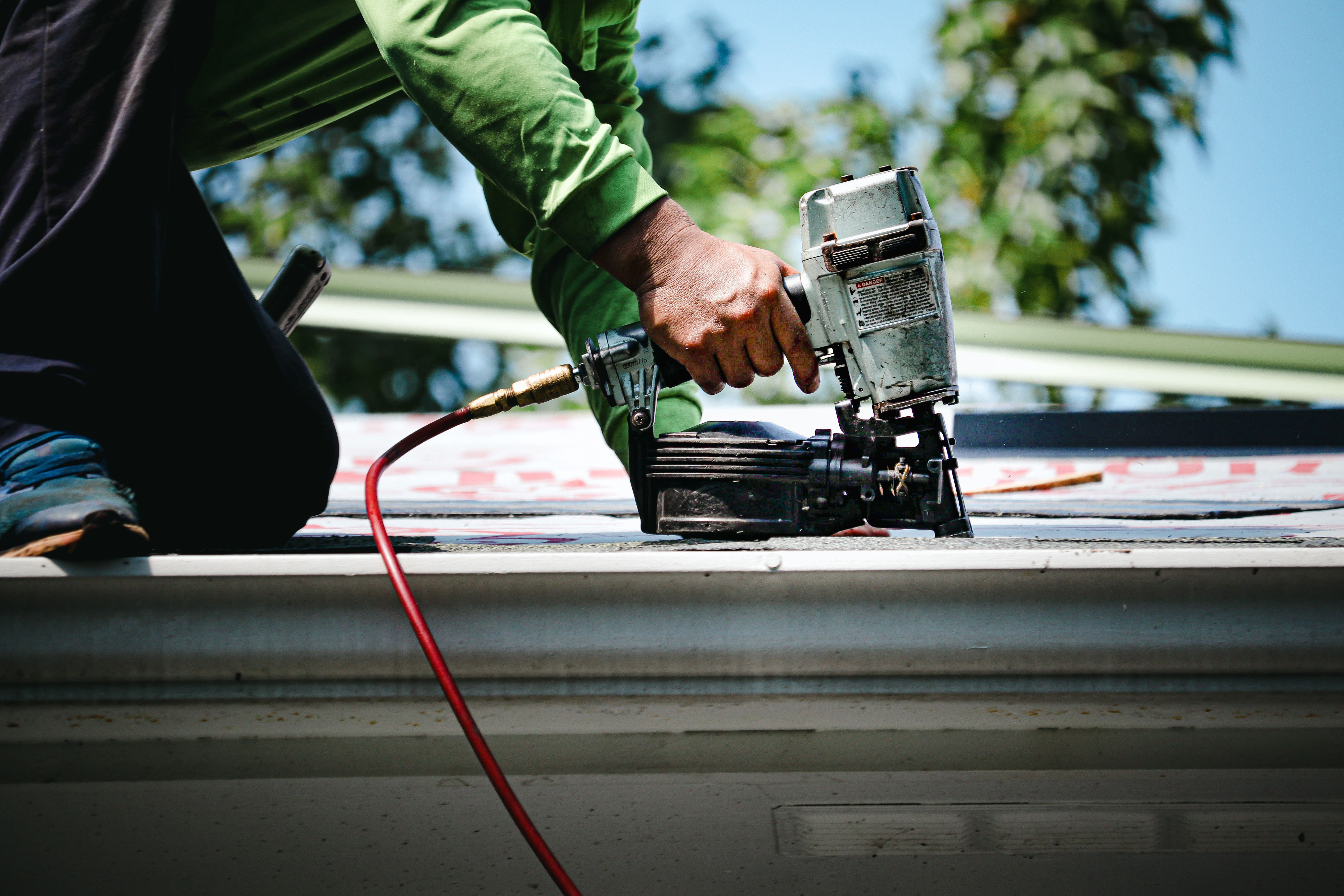 Roofer using nail gun to fix shingle at roof edge