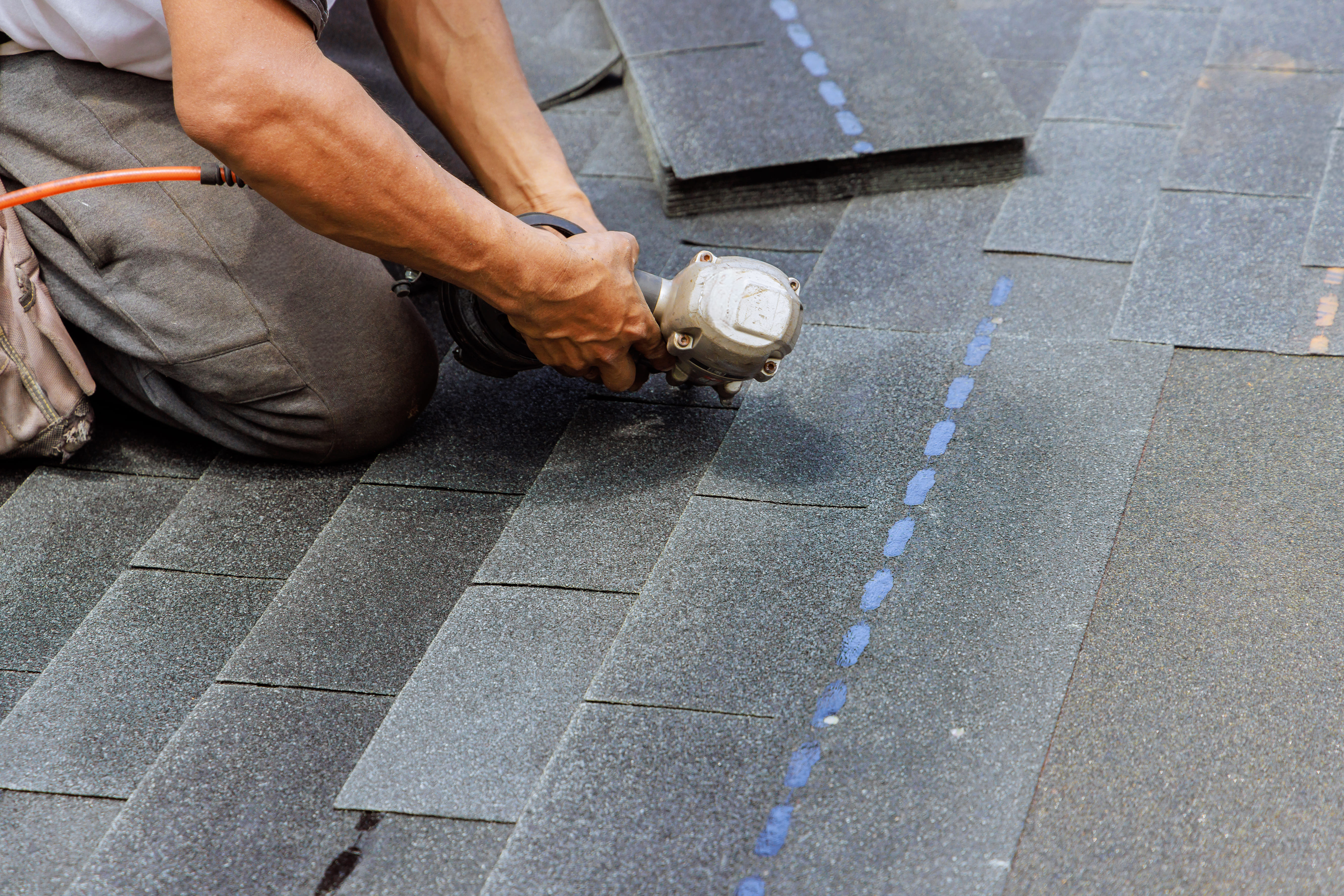 Close-up of nail gun on roofing shingles with chalk line