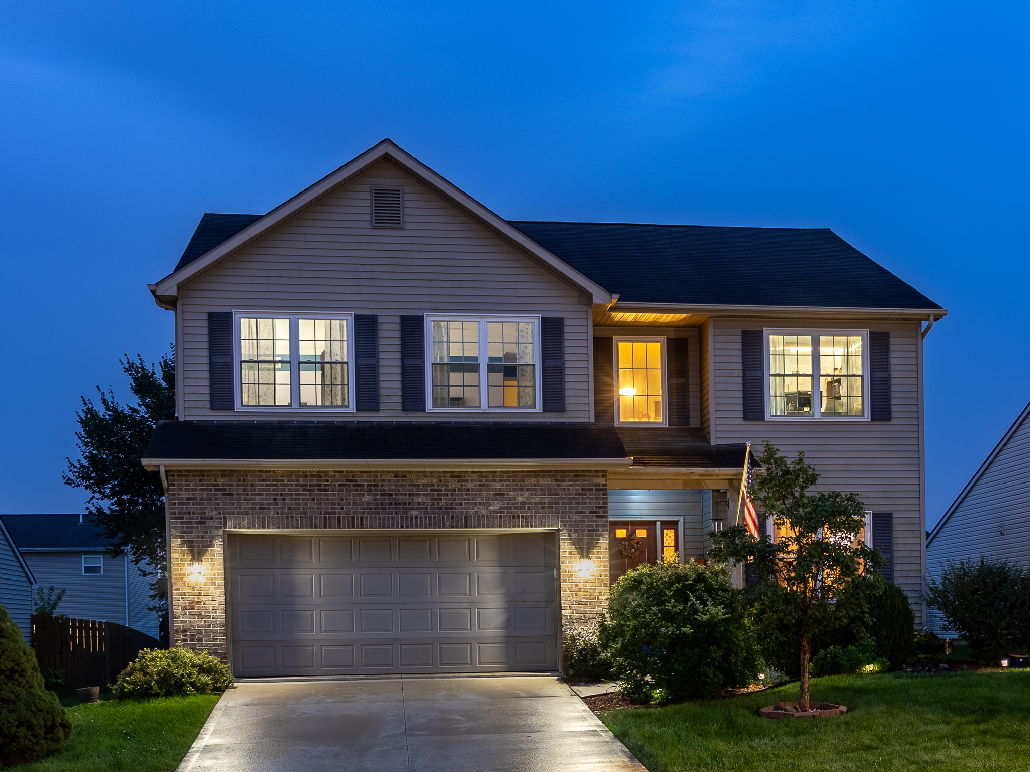 Twilight exterior of a two-story home with interior and exterior lights glowing.
