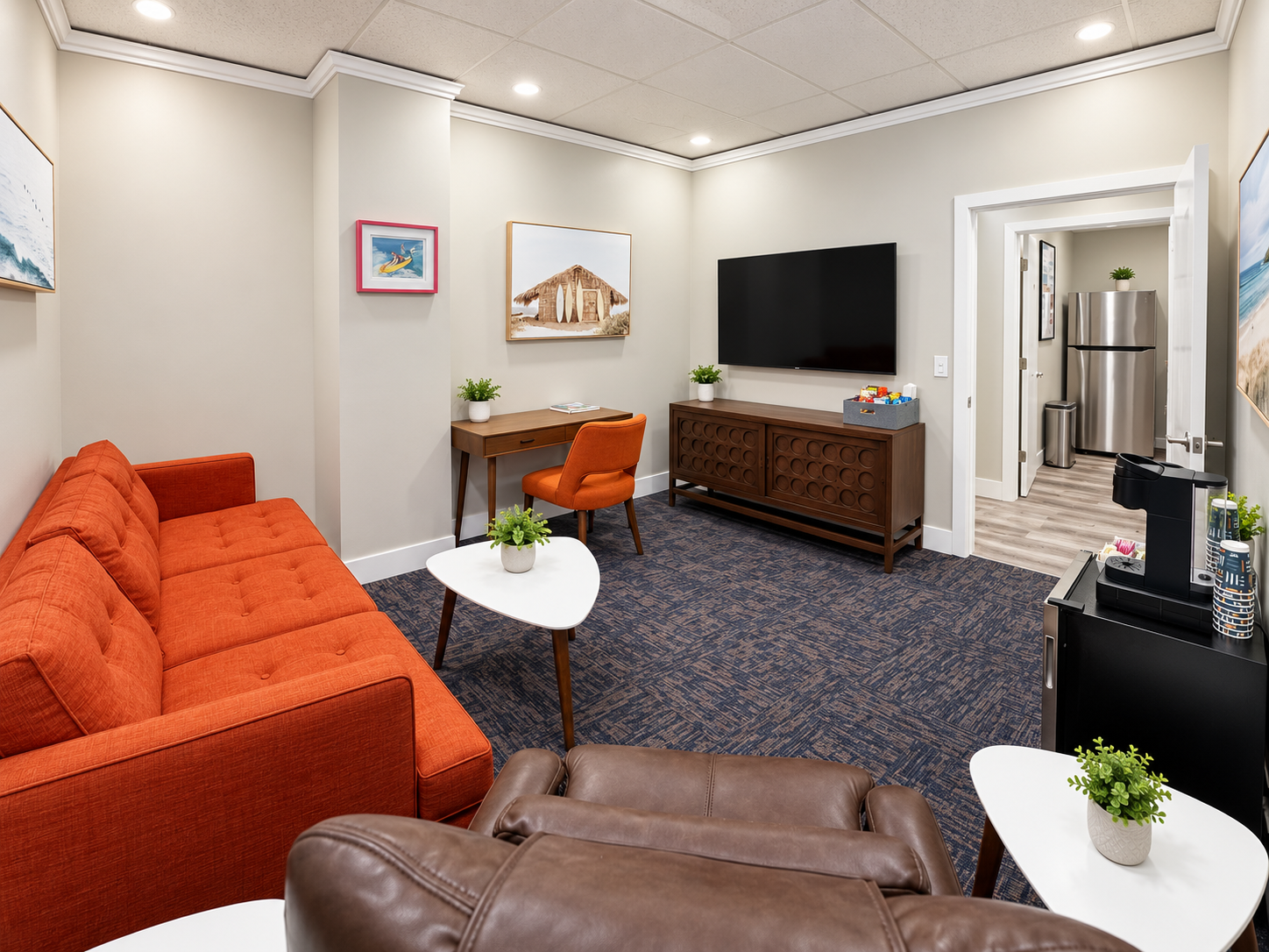 Private suite with work desk, orange couch, smart TV, and kitchen dining area in the SAINT Lounge Wing