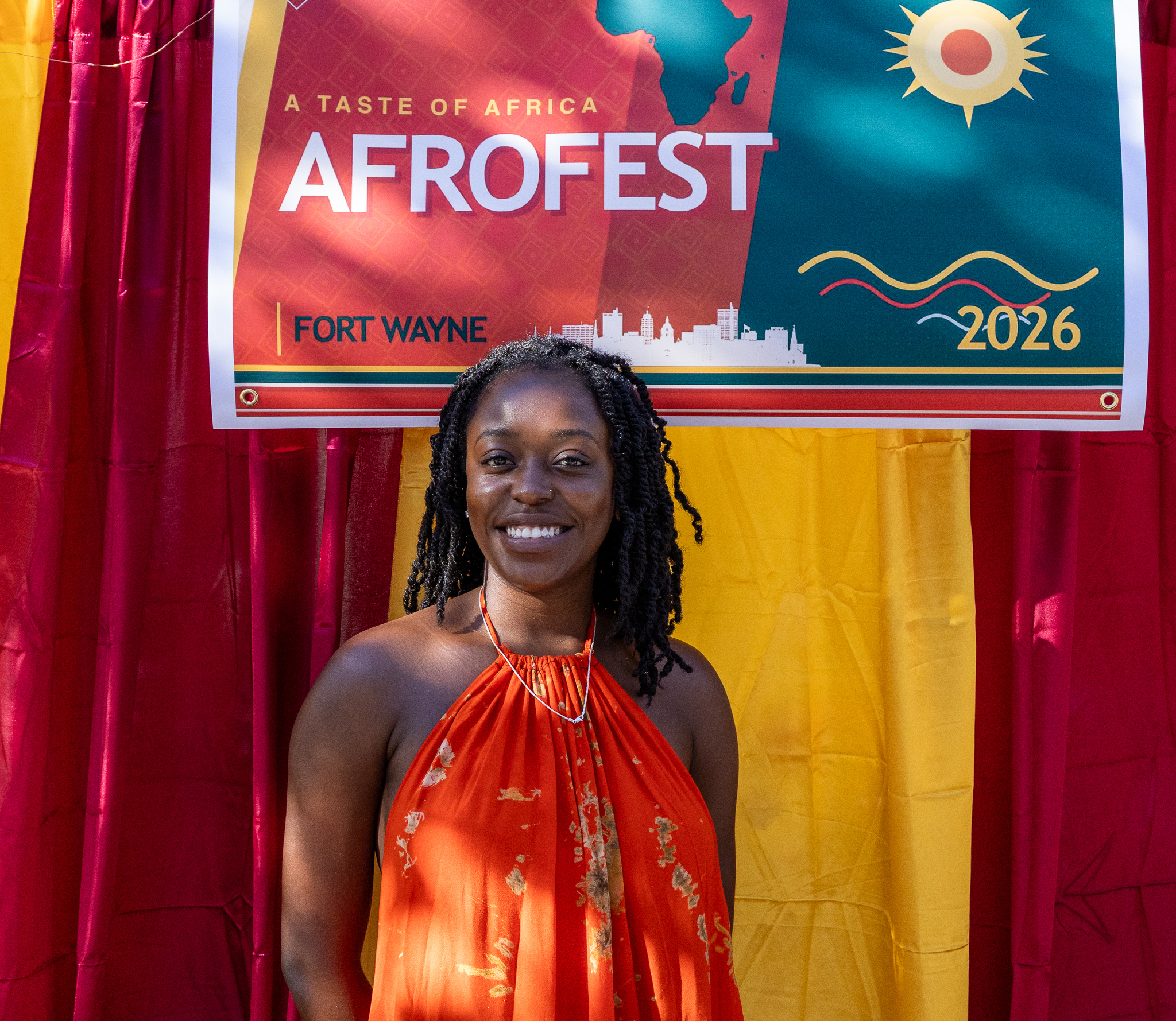 Smiling attendee in vibrant orange halter dress at the Afrofest 2026 backdrop