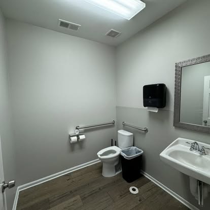 Commercial ADA accessible bathroom renovation with stainless grab bars, vanity, and waterproof flooring