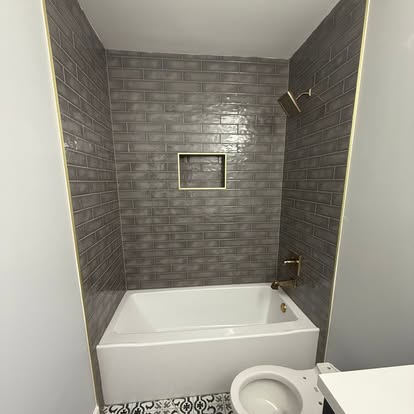 Modern bathroom remodel with gray stacked subway tile shower surround, brass fixtures, and recessed niche