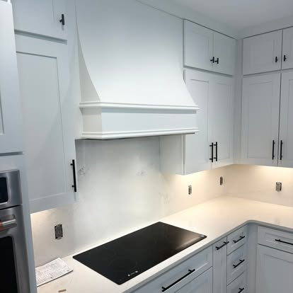 Custom flared range hood and quartz backsplash installation in modern white kitchen