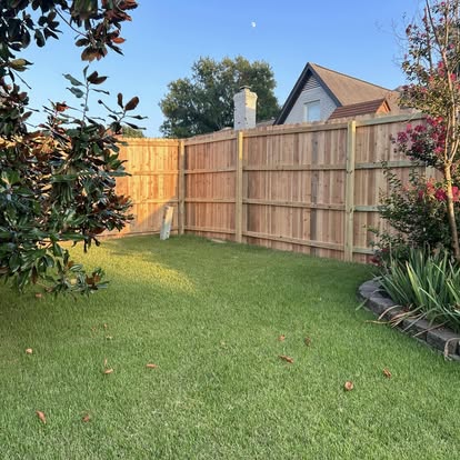 Straight and plumb residential wood privacy fence along green lawn and garden