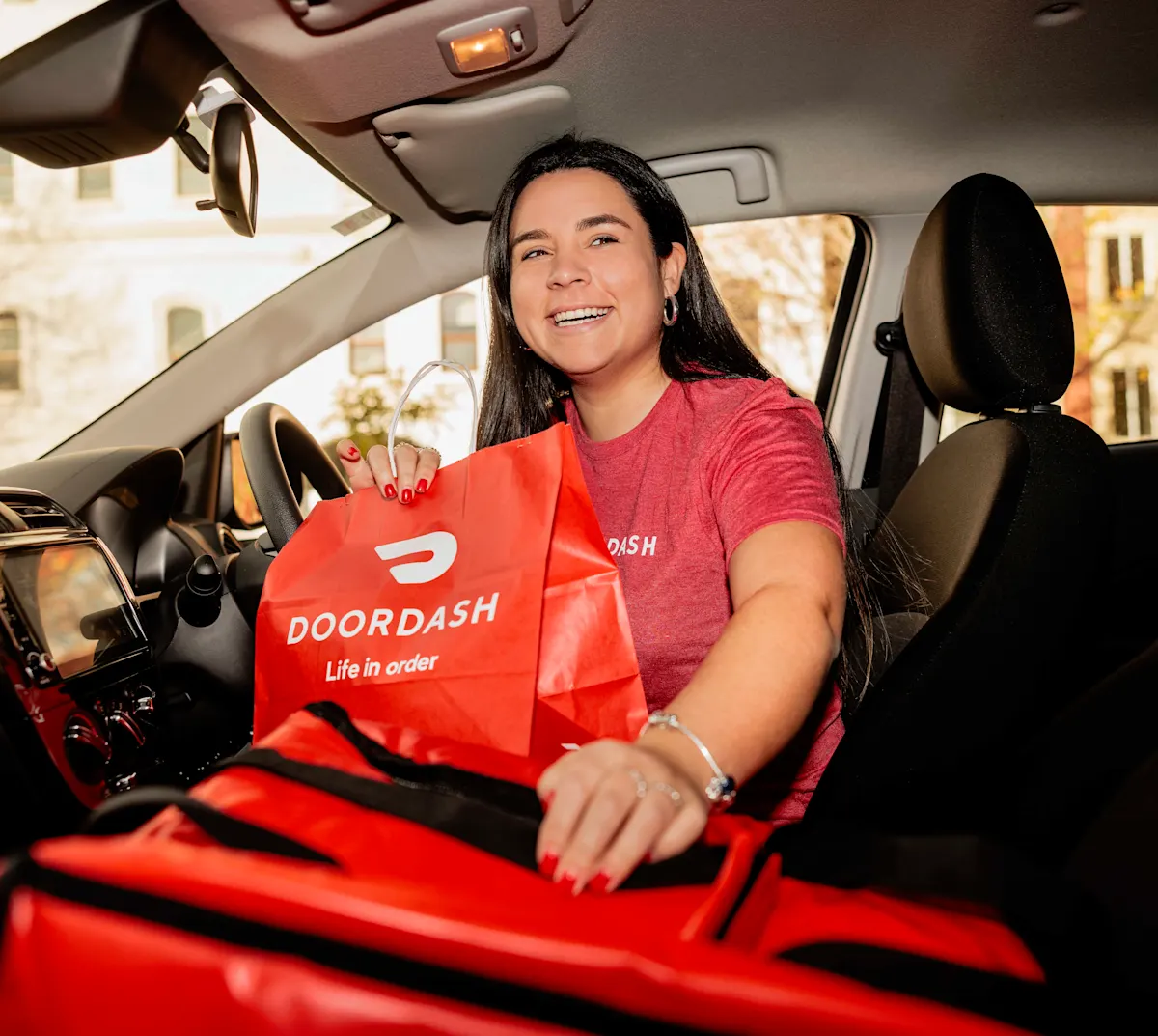 DoorDash delivery driver holding branded delivery bag inside a reliable sedan vehicle for rideshare and delivery work in Calgary