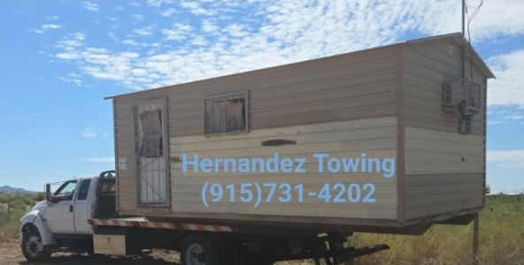 Hernandez Towing flatbed transporting a wooden shed structure through rural Texas landscape