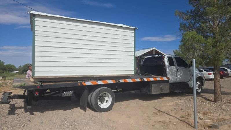 White metal storage building being transported on Hernandez Towing flatbed truck