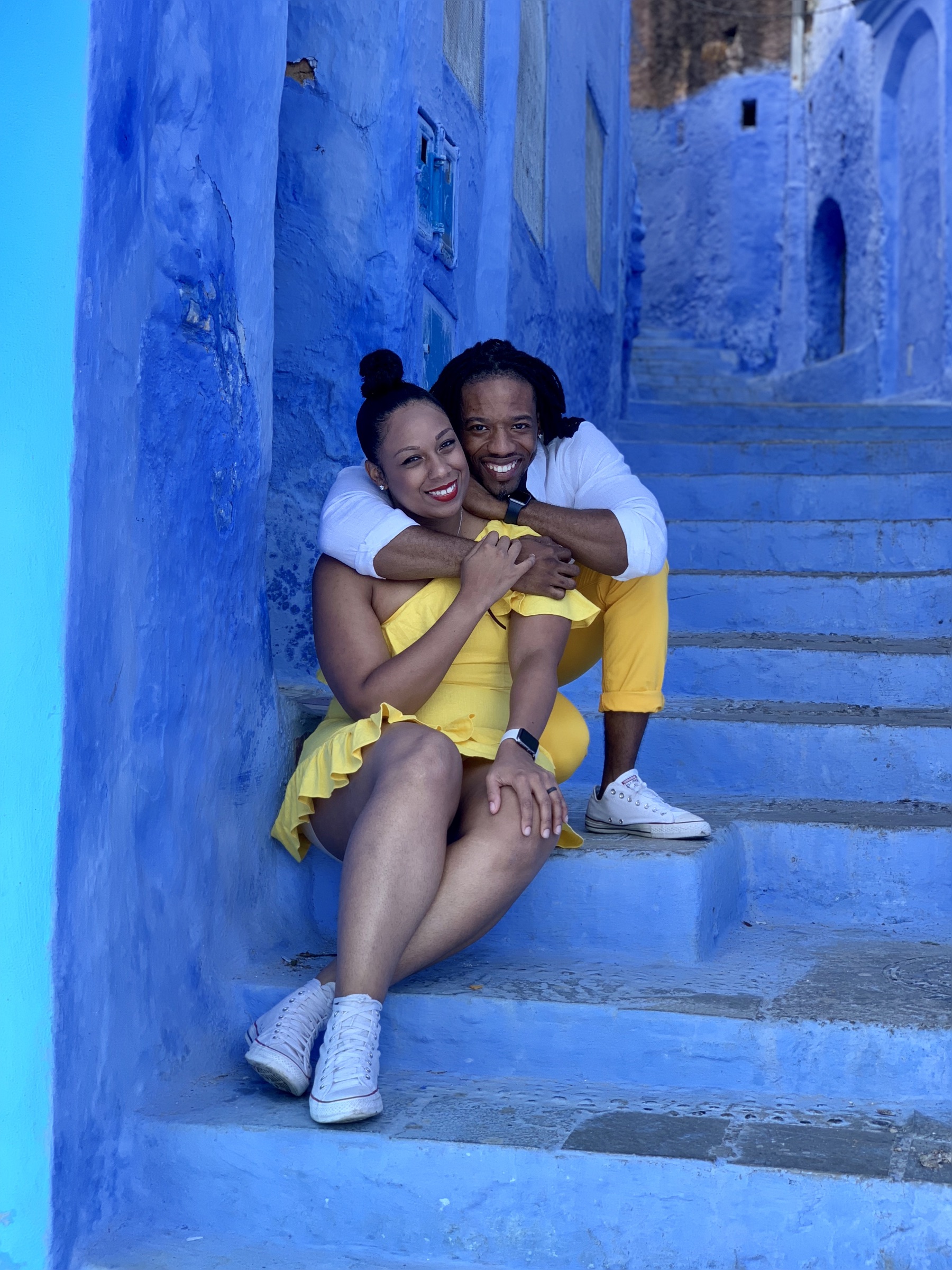 Kes and Jaz sharing a warm embrace on blue steps.