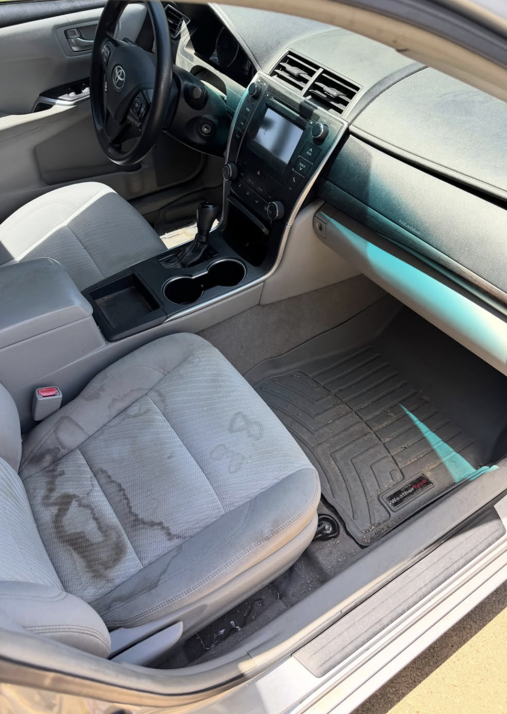 Severely stained sedan cloth seat and dirty weather floor mat before interior detailing
