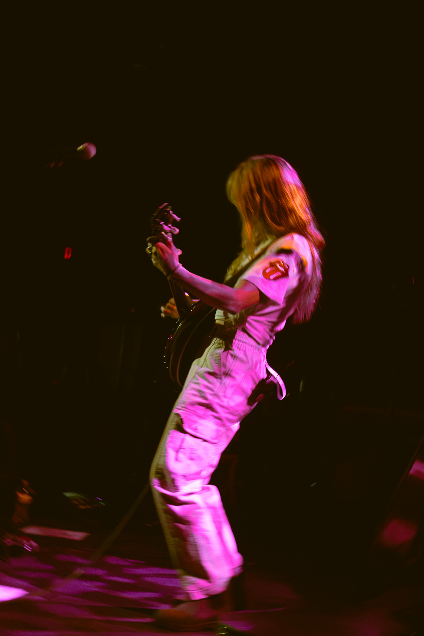 Brenna MacMillan performing live in Rolling Stones patch shirt under pink stage lights at The Waiting Room