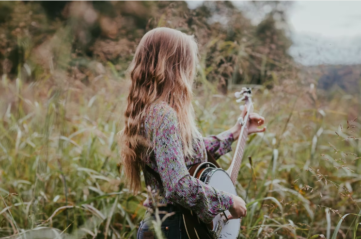 Brenna MacMillan from behind playing banjo in tall grass field