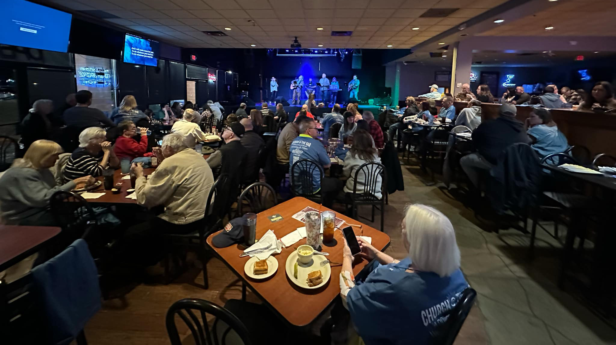 Church at the Bar community gathered inside Brewskeez with a band on stage and people sitting at tables with food and drinks