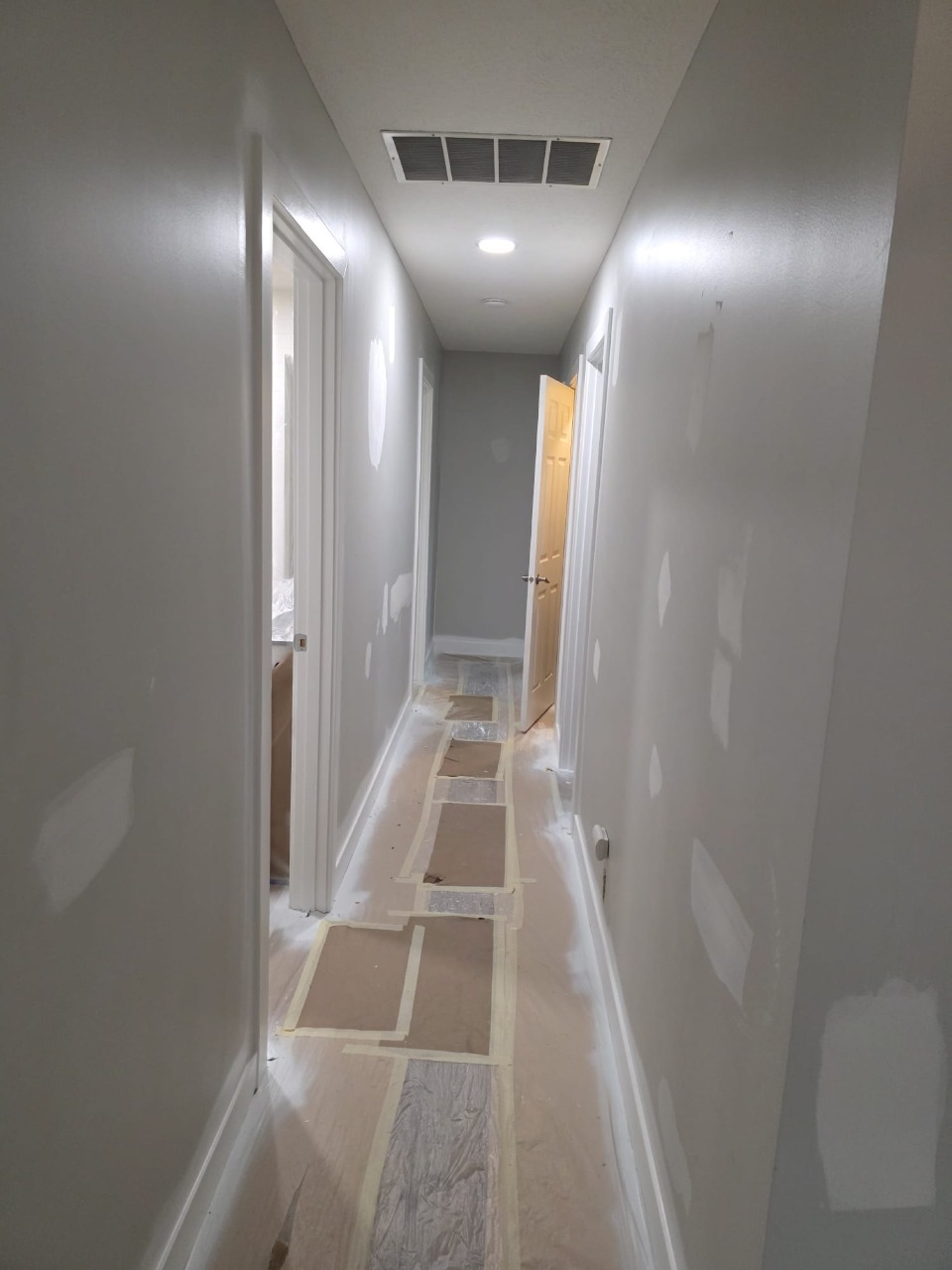 Hallway with patched walls and protective floor covering during professional paint preparation phase