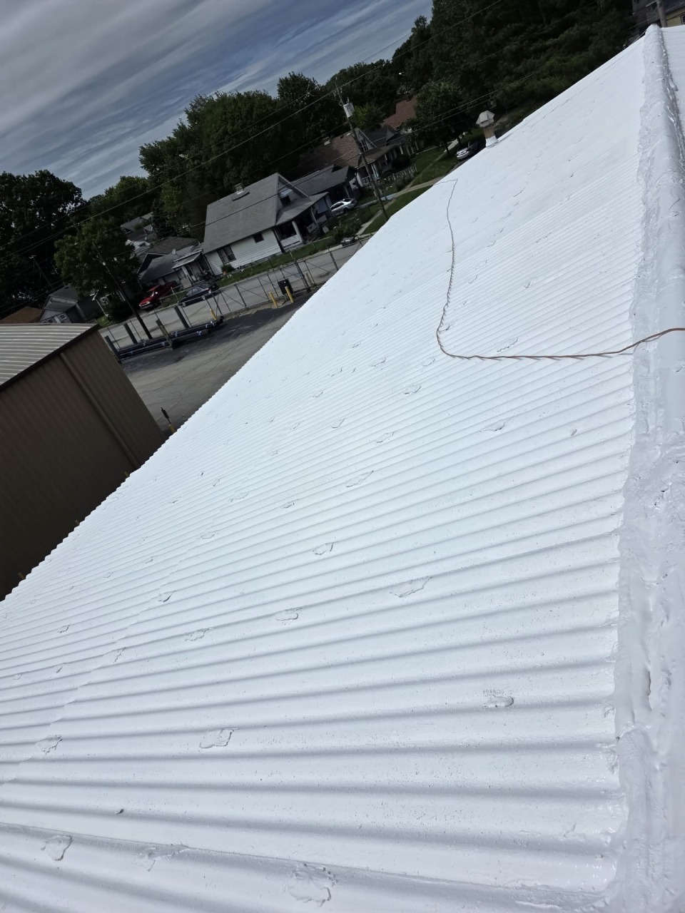 Wide view of white coated metal roof showing smooth even finish across entire surface with residential neighborhood backdrop