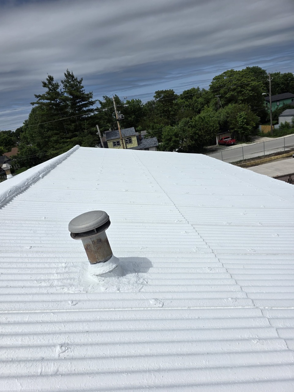 White coated metal roof with vent pipe properly sealed and painted, showing quality craftsmanship on roof penetrations