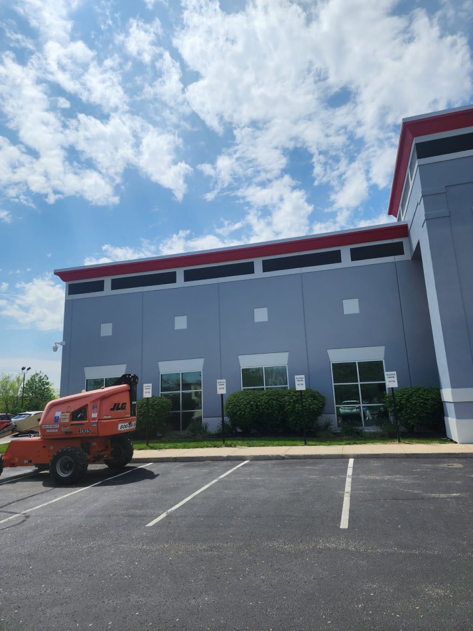 Large commercial building exterior freshly painted in gray with red trim accents, featuring multiple windows and professional finish