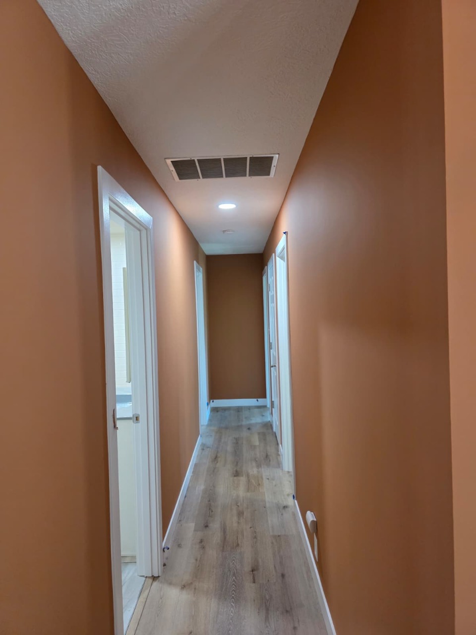 Finished hallway with beautiful warm terracotta orange walls, white trim, hardwood floors, and recessed lighting