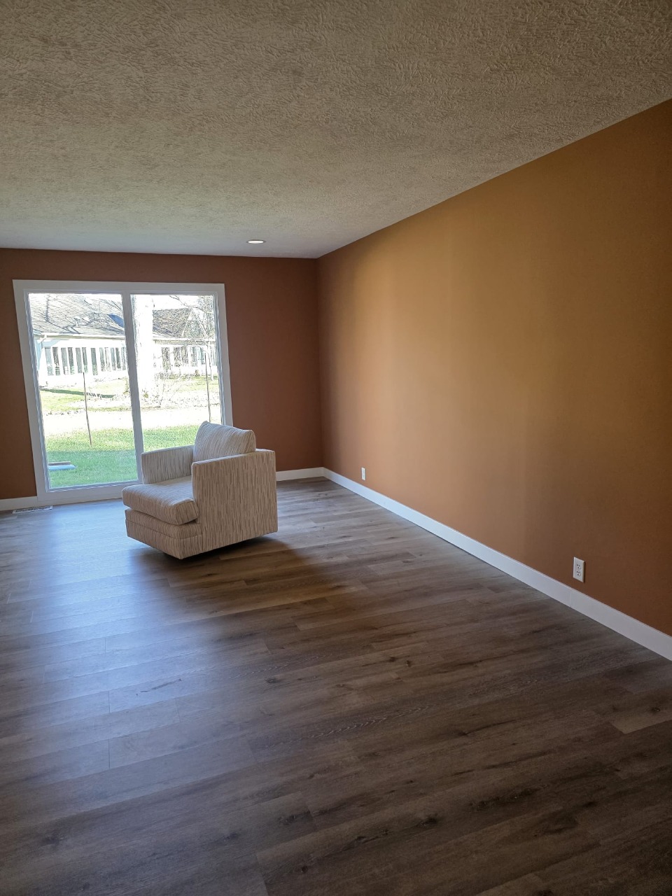 Completed living room transformation with warm terracotta orange walls, white trim, hardwood flooring, and sliding glass door to backyard