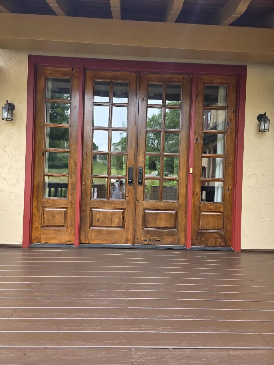 Wooden French doors with rich burgundy red trim and cream stucco walls on covered porch with lantern lighting
