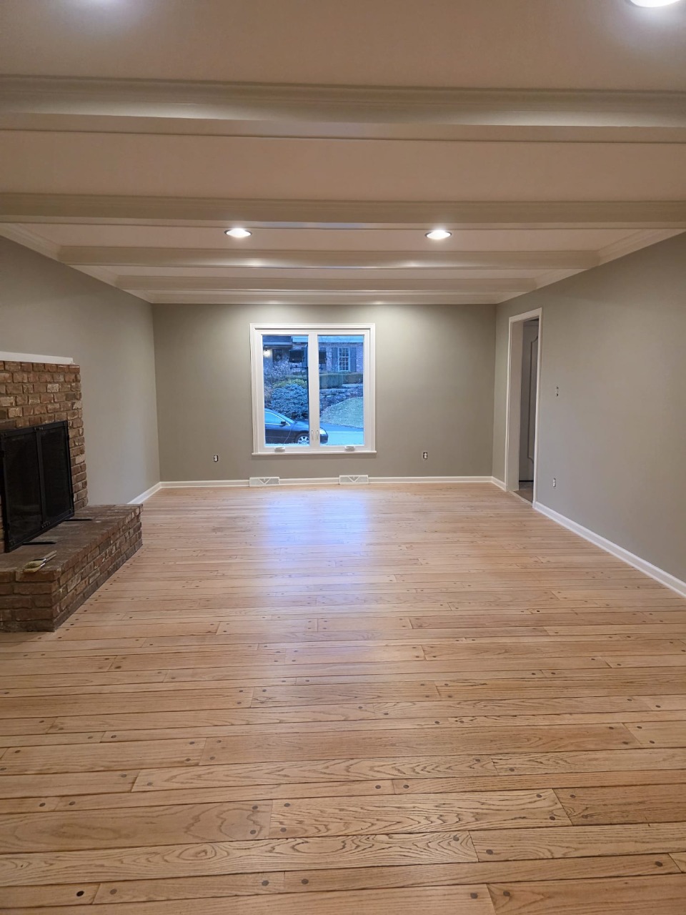 Spacious living room with gray walls, hardwood floors, and brick fireplace