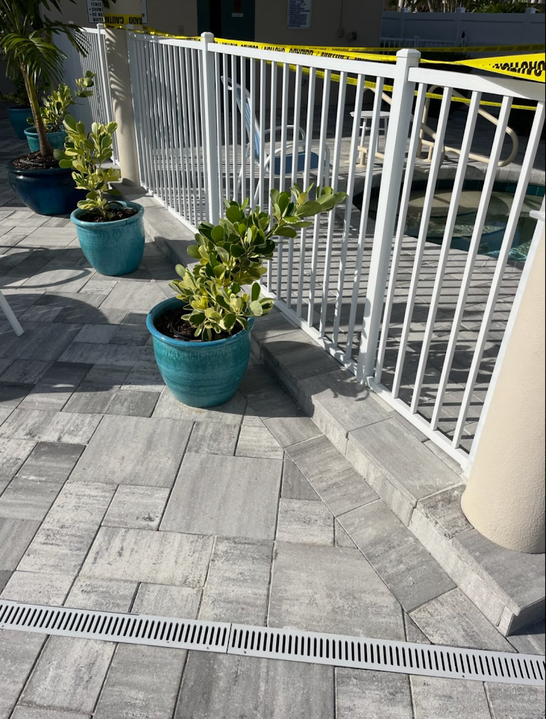 Pool deck paver installation with white safety railing and decorative planters